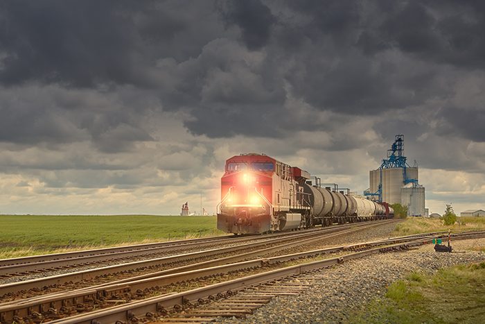 Red freight train with grain elevators and storage bins on the prairie. Dramatic sky with lots of copy space. (Please see my portfolio for related photos and video clips).