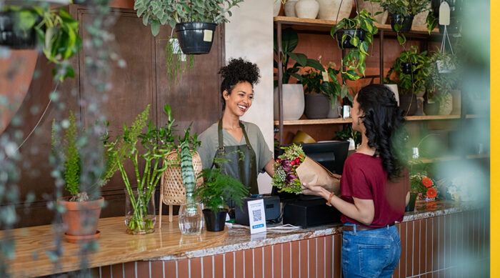 Flower shop business owner assists a female customer at a reception desk.