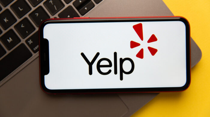 Yelp logo on a smartphone next to a gray laptop computer.