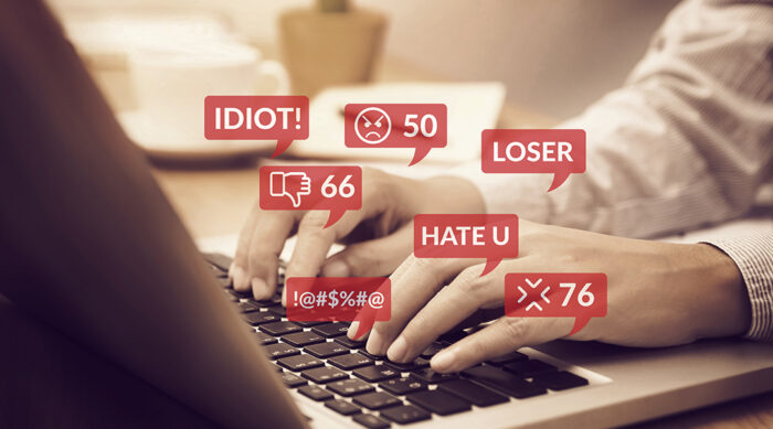 Person using a laptop keyboard with hurtful words and phrases.