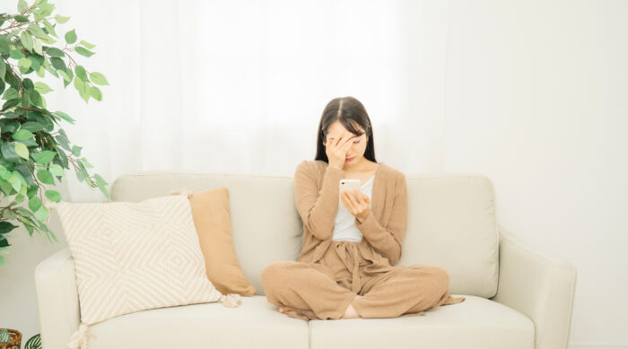 Woman sits cross legged on a tan couch with a hand to her face after being targeted for defamation.