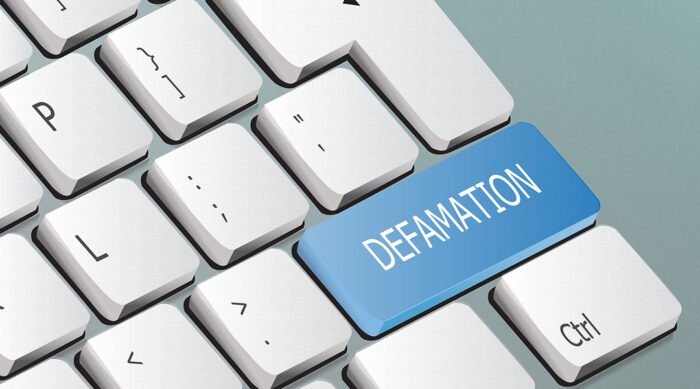 A white computer keyboard with a blue key with the word defamation on it.