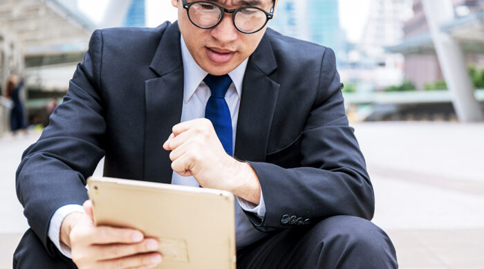 A businessman sits outside and reads a claim of online defamation on a tablet.