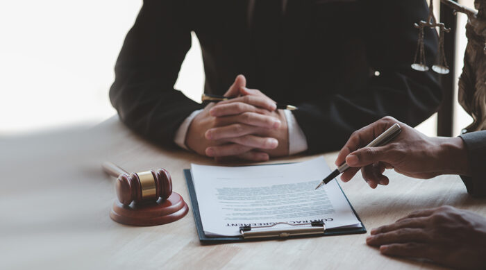 Two male attorneys sit at a wooden conference table and review libel vs. slander defamation.