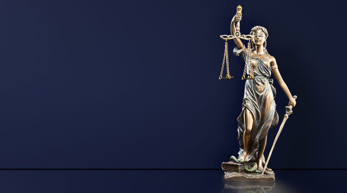 Small Lady Justice statue on a table with a bright navy background.