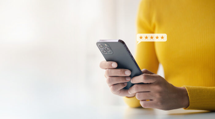 Woman wearing a bright yellow sweater reads online customer reviews on a smartphone.