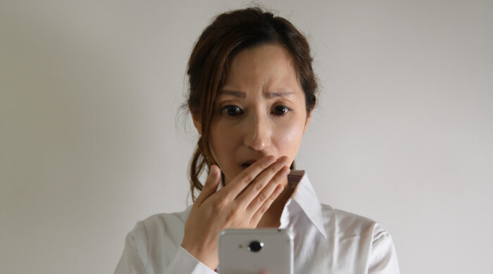 Woman holds her hand over her mouth and gasps while looking at a mobile phone.