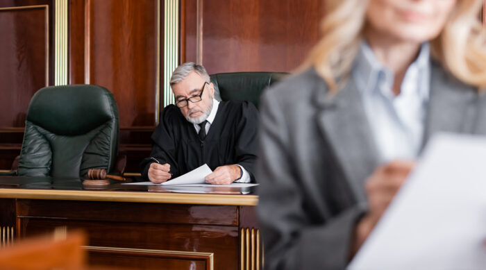 A female attorney stands in a courtroom as a judge reviews a defamation lawsuit.