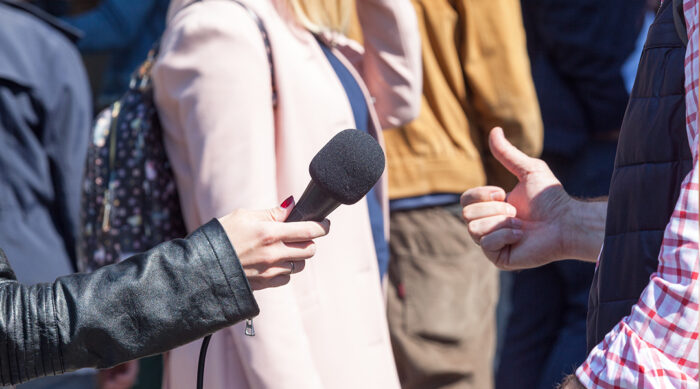 Journalist holds a black microphone while interviewing a male public figure.