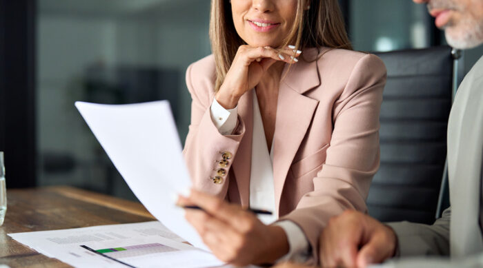 Female attorney in a pink blazer reviews court documents to support a defamation case with her client.