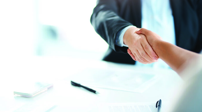 Two business people shaking hands over documents, symbolizing trust and agreement when using representations and warranties insurance in business deals.
